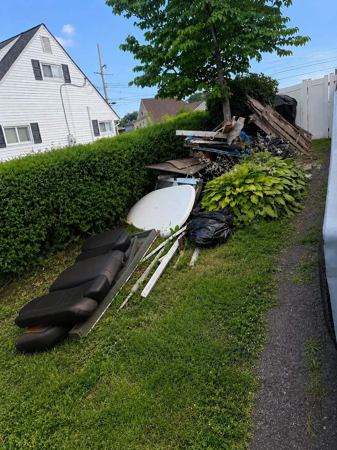 Side yard piled with debris along the hedge line before junk removal